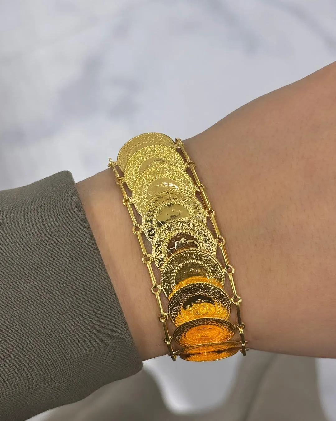 Breites Armband aus überlappenden Goldmünzen zwischen zwei Gliederketten am Handgelenk